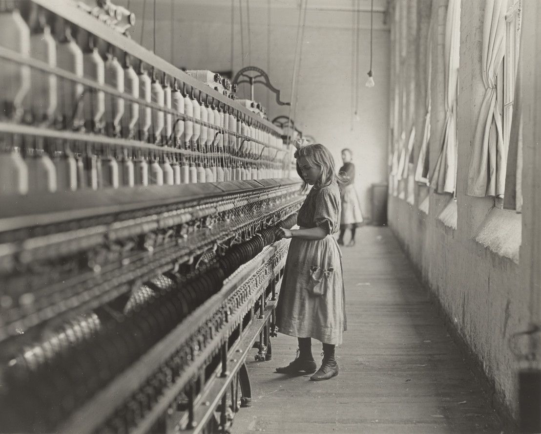 A young girl working at a textile mill in early 20th-century America, part of Lewis Hine's child labor documentation. before enhancement and upscaling