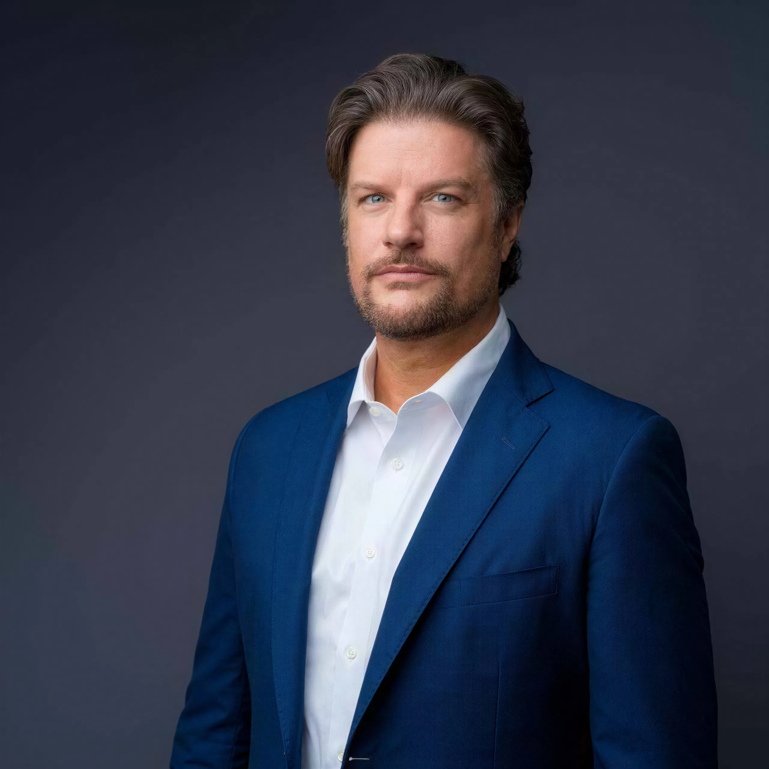 Studio headshot of a man in a navy suit upscaled with identity and lighting kept intact after enhancement and upscaling
